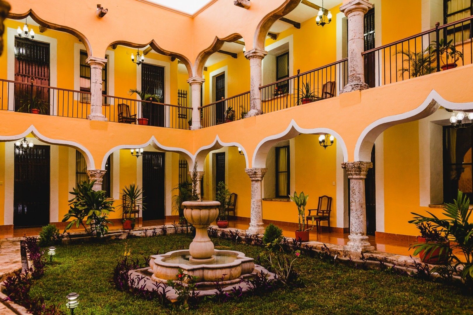 Patio con paredes amarillas, columnas blancas y fuente.