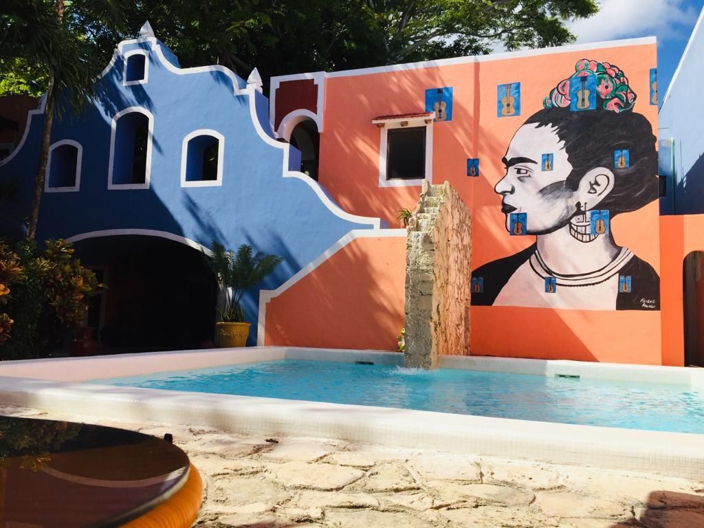 Edificio colorido con mural de Frida Kahlo junto a una piscina.