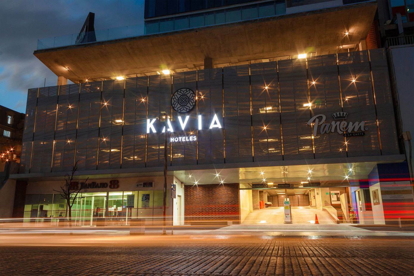Fachada del edificio con el cartel "KAVIA by STYLY" iluminado, entrada debajo, escena nocturna.