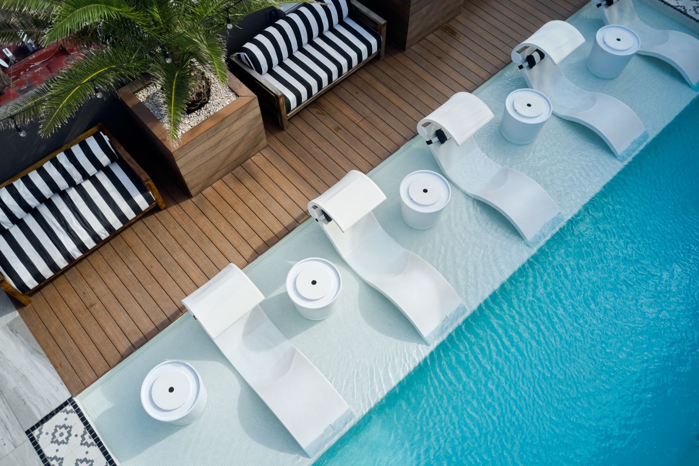 Zona de salón junto a la piscina con tumbonas blancas, asientos a rayas y una piscina azul.