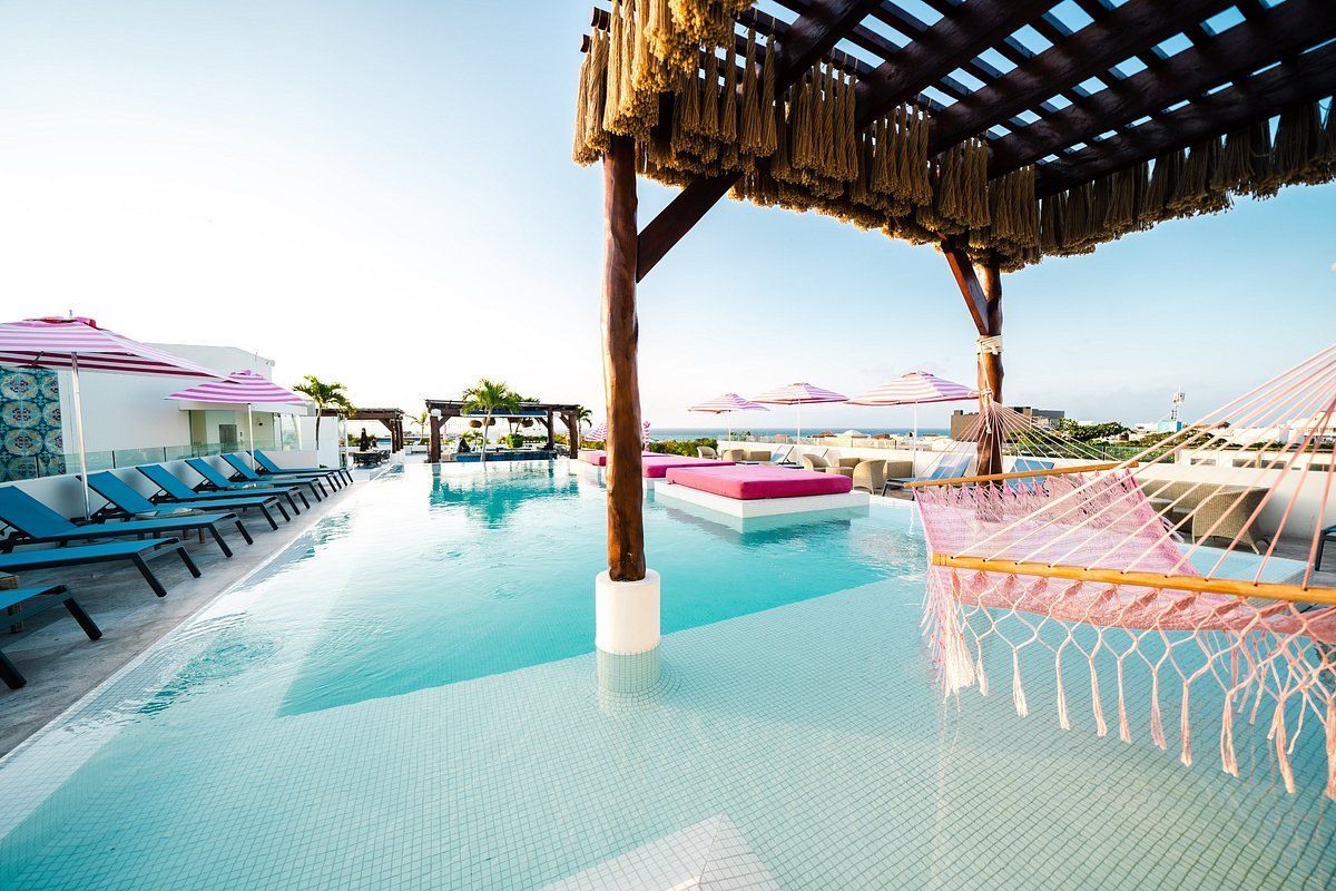 Piscina en la azotea con agua turquesa, tumbonas y una hamaca rosa bajo una pérgola de madera.