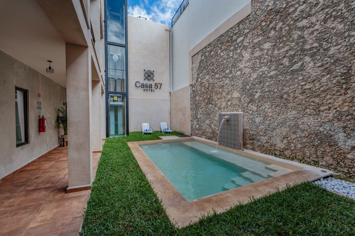 Pequeña piscina en un patio del hotel Casa 67 con muro de piedra y ascensor.