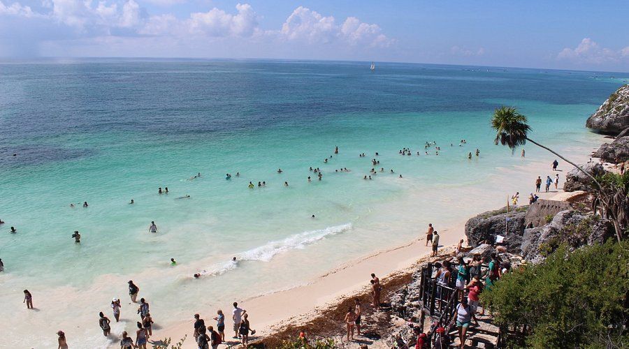 Personas nadando en aguas turquesas en una playa con vista al acantilado, Tulum, México.