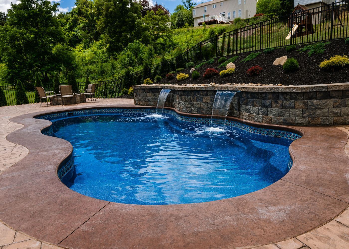 Swimming pool with waterfalls, surrounded by a stone wall and landscaping.