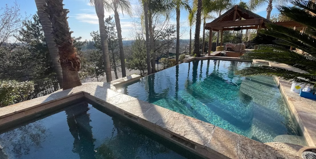 Swimming pool and spa with gazebo in a sunny outdoor setting with palm trees.