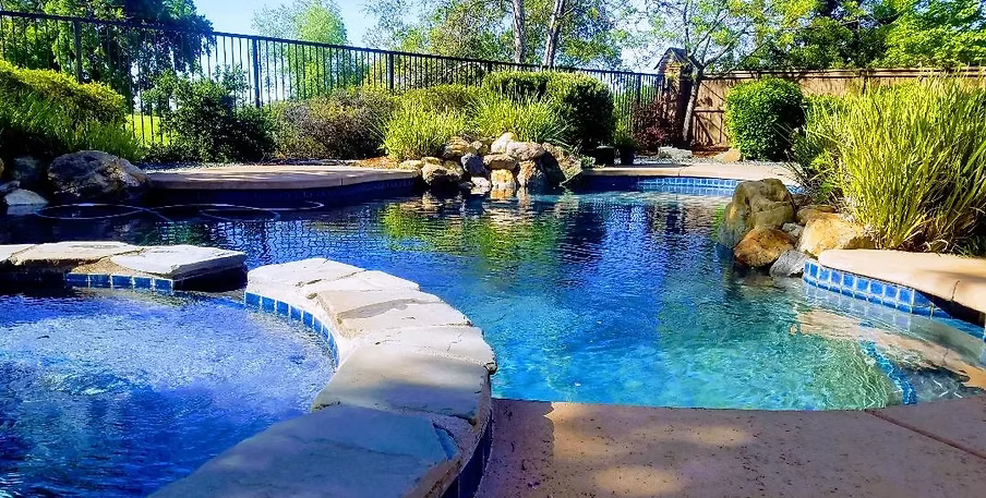 Swimming pool with stone walkways, blue water, and landscaping.