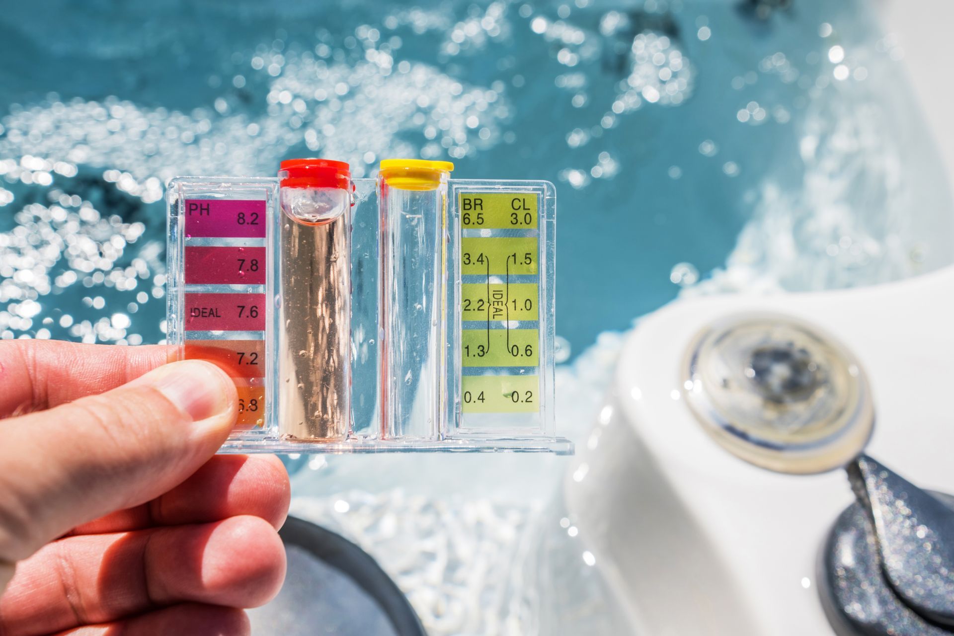 Hand holding a pool water test strip beside a hot tub, with colored test vials visible