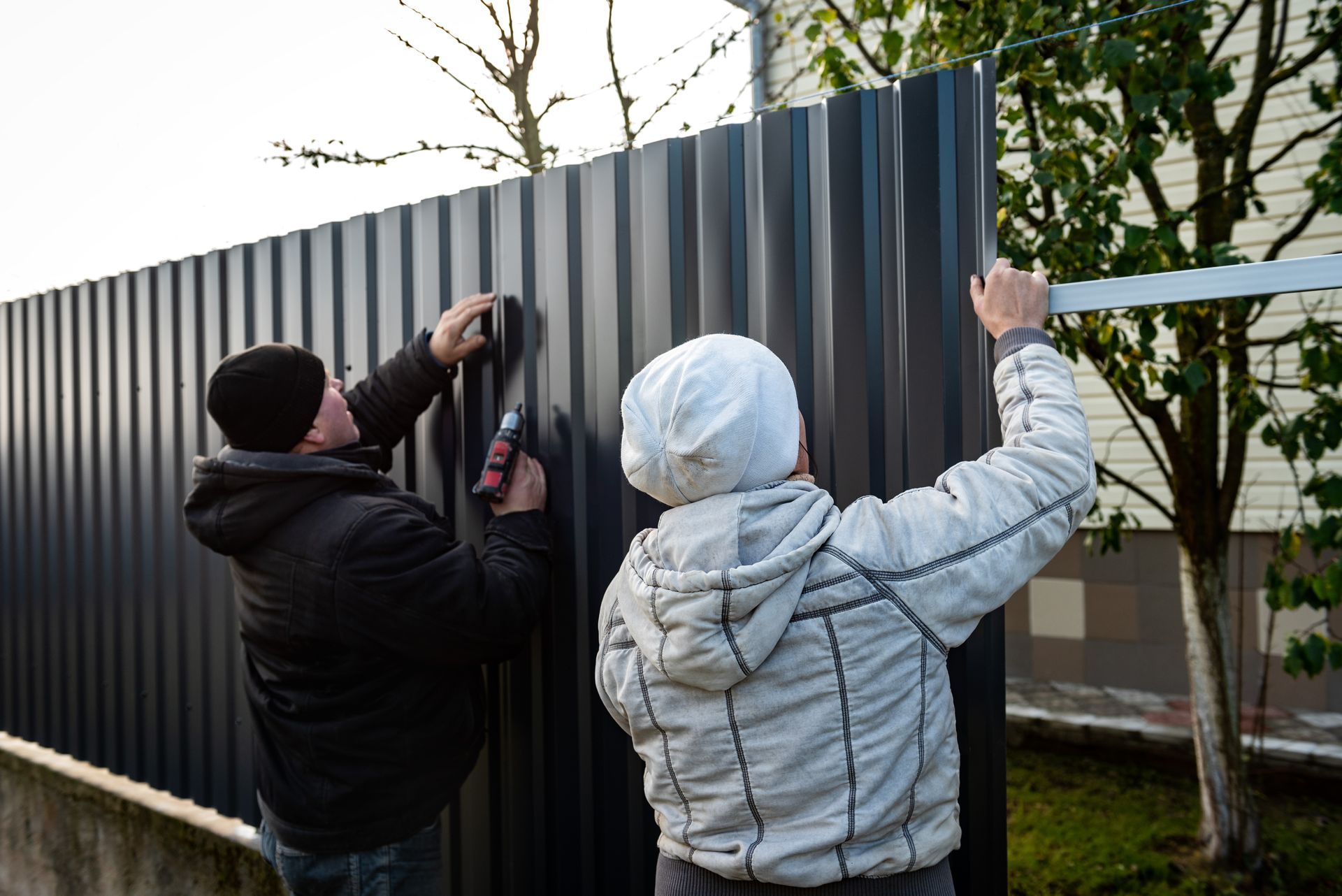 Workers using a drill to install a metal fence, providing an expert commercial fencing installation. Workers using a drill to install a metal fence, providing an expert commercial fencing installation.