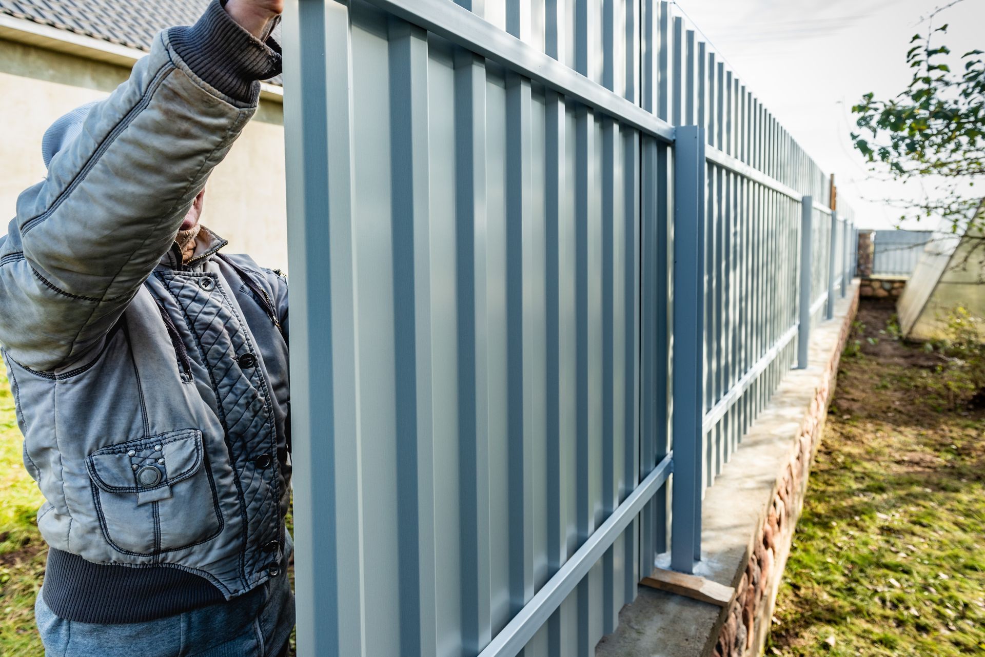 A worker installs a corrugated metal fence during a professional commercial fencing installation.