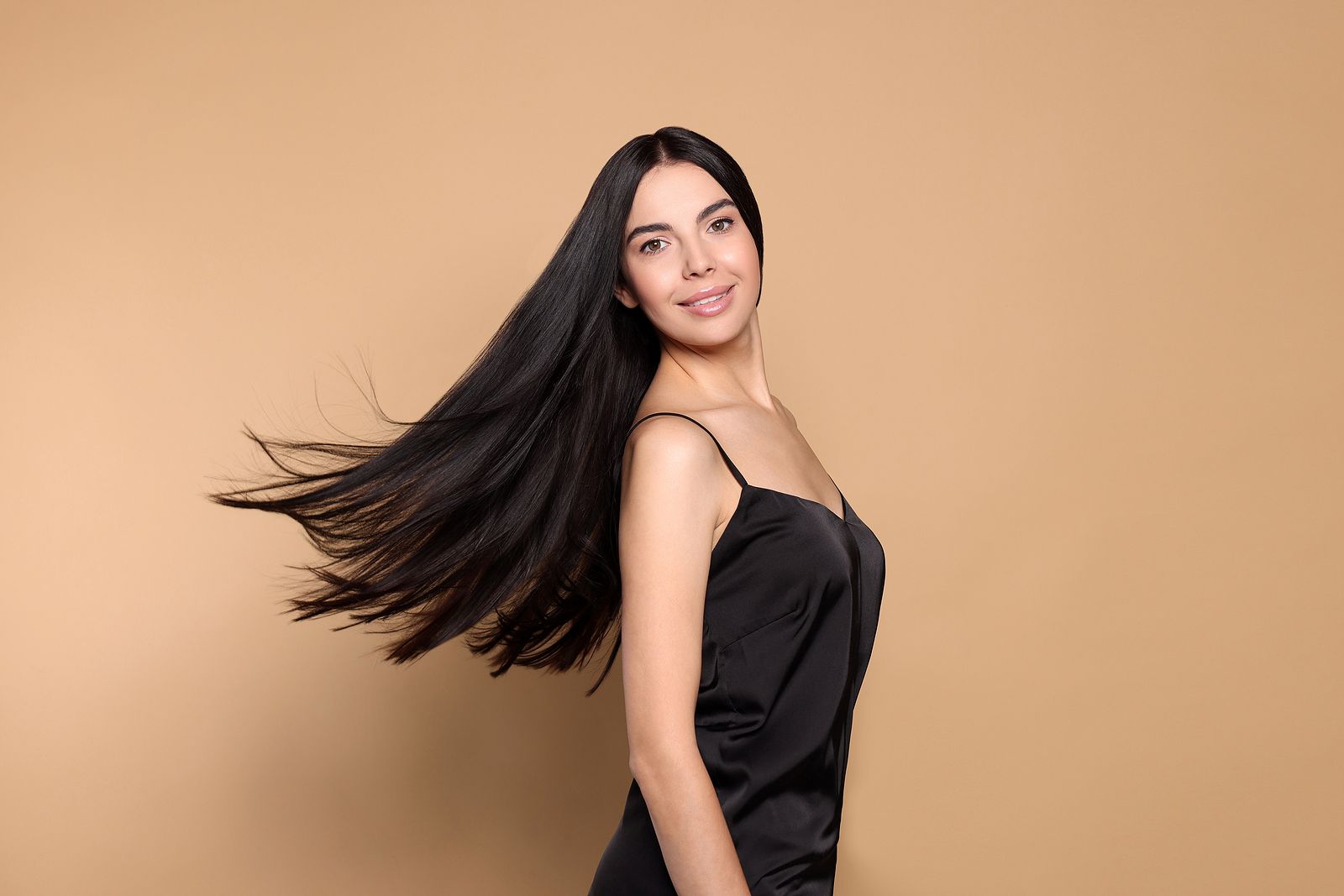 The woman is wearing a black dress and her hair is blowing in the wind.