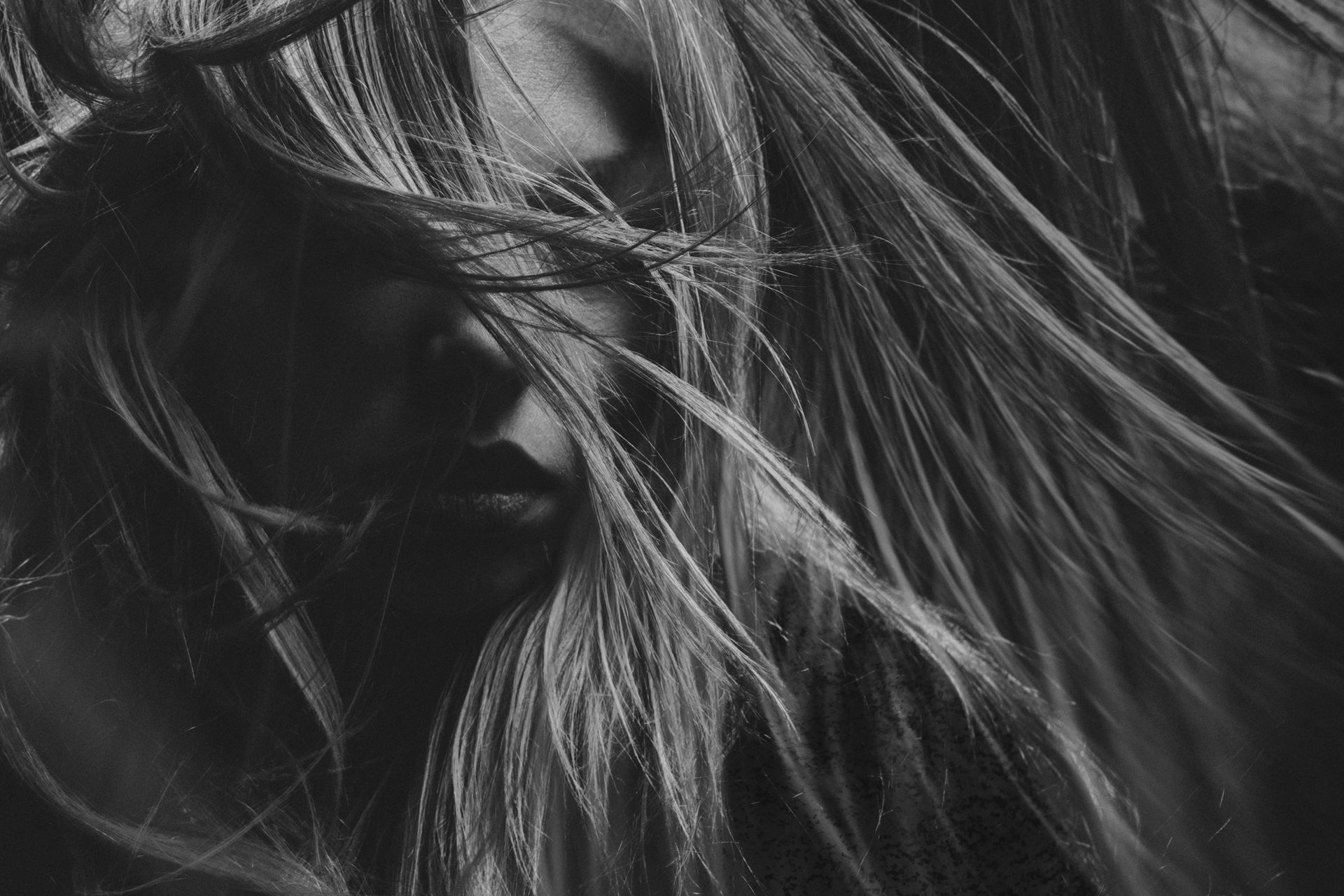 A black and white photo of a woman 's hair blowing in the wind.