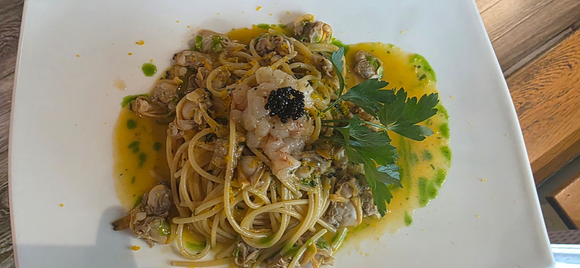 Un piatto di pasta con vongole, un gambero e una cucchiaiata di caviale in una salsa leggera e burrosa, guarnito con erbe aromatiche fresche.