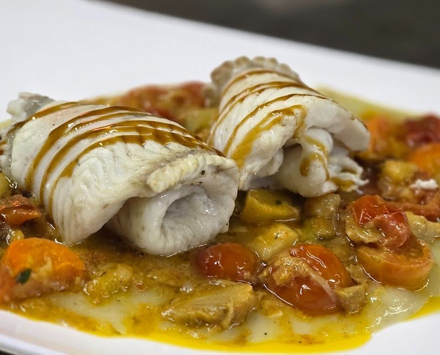 Due filetti di pesce bianco arrotolati e conditi con salsa, serviti su un letto colorato di pomodorini e verdure saltate.