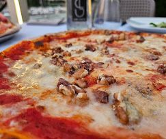 Primo piano di una pizza condita con formaggio bianco fuso e noci, servita su un tavolo di un ristorante.