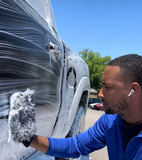 A man in a blue shirt is washing a truck with a glove.