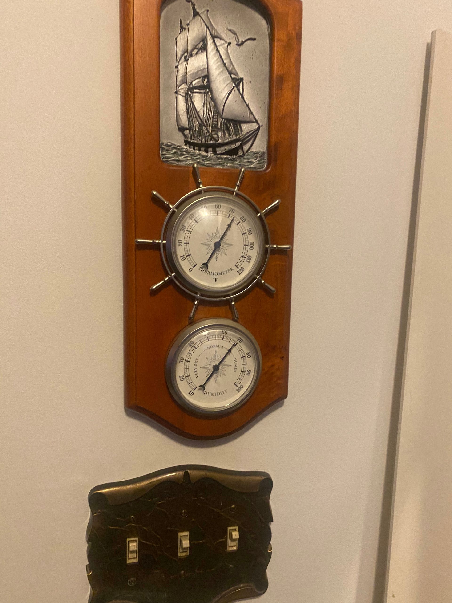 Wooden nautical wall decor with ship, clock, thermometer, and coat rack.
