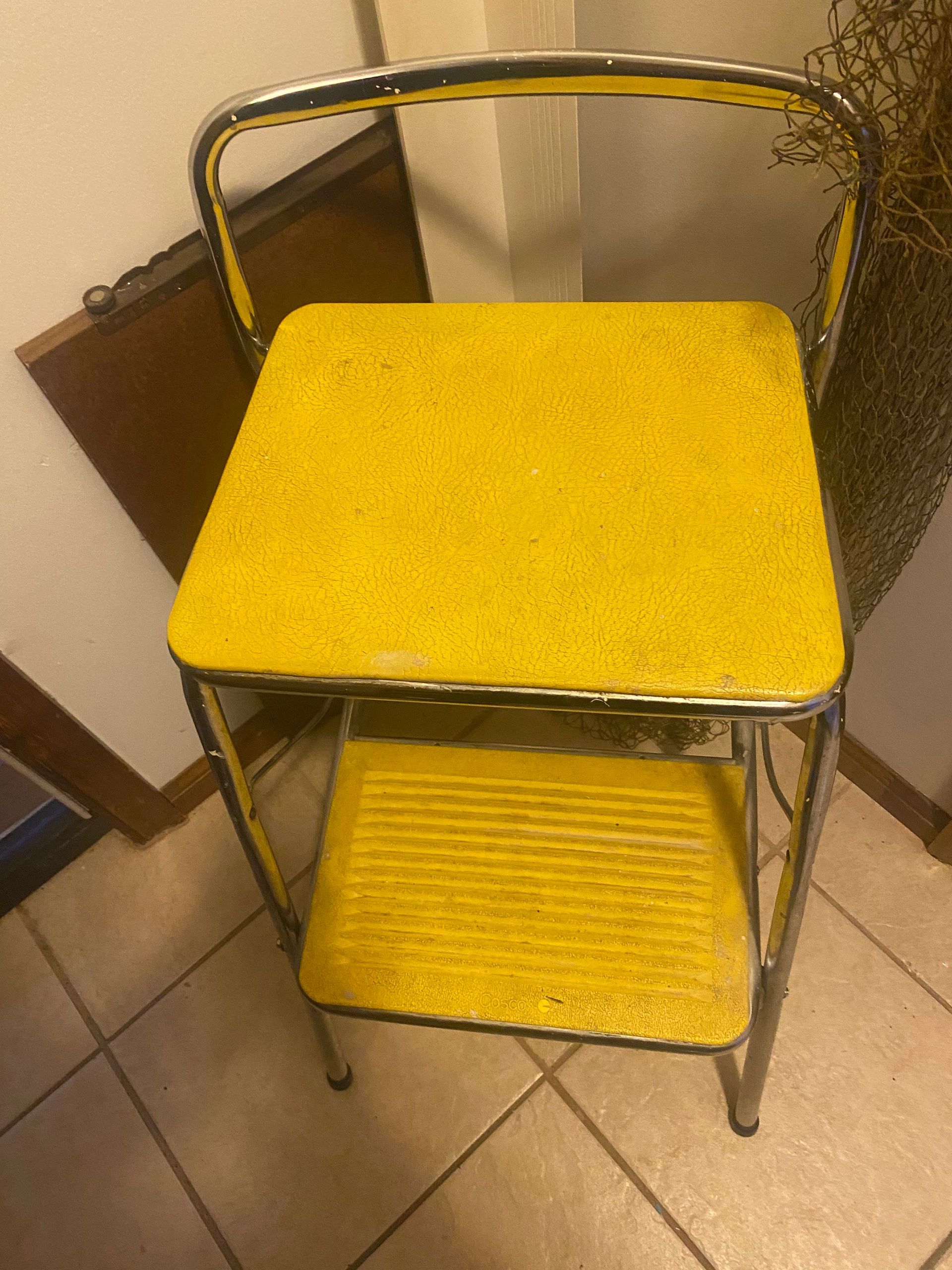 Yellow and chrome retro step stool against a corner wall.