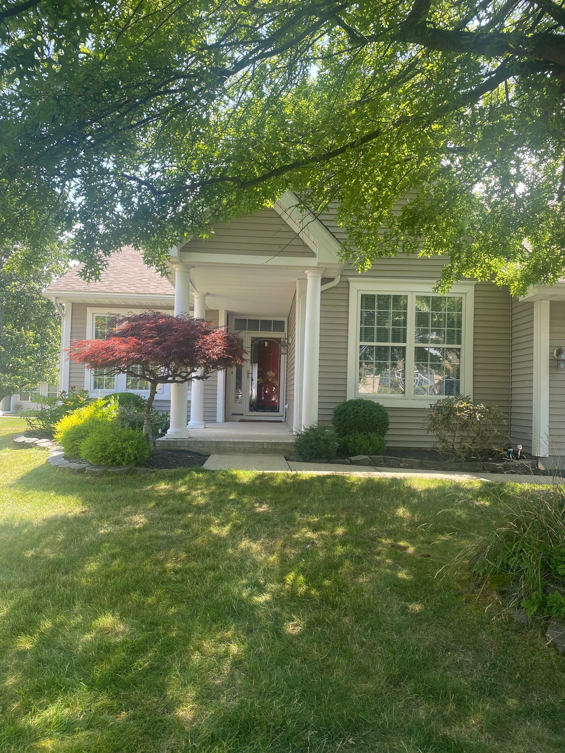 Beige house with a covered porch and red front door, framed by trees and a green lawn.