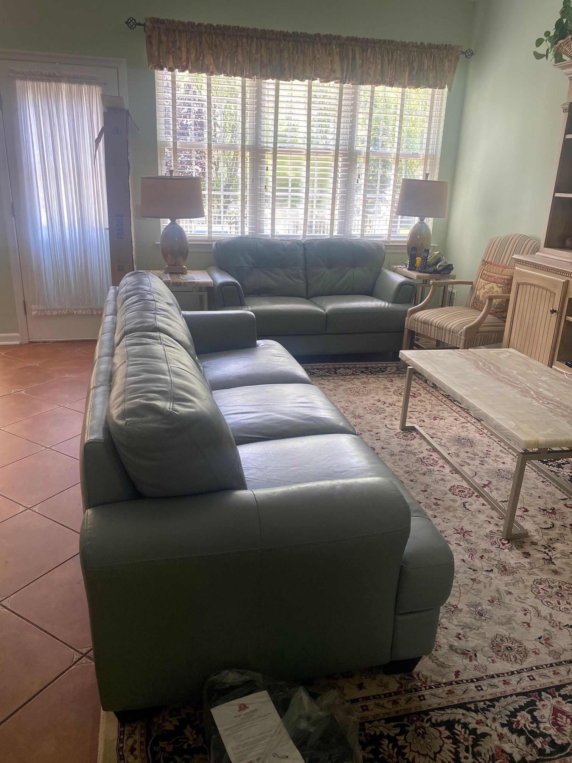 Green leather sofas in a living room with a window, lamps, and a rug.