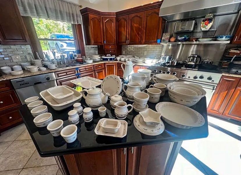 Kitchen with many white dishes on counter and cabinets. Appliances in the background. Sunlight.