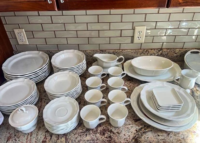 White ceramic dishes on a countertop: plates, bowls, cups, gravy boat, sugar bowl, and serving platters.