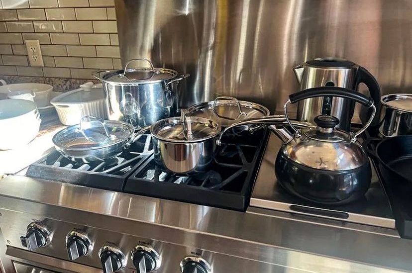 Stainless steel pots and kettle on a gas stovetop in a kitchen.