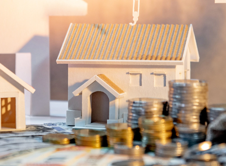 Miniature white house model with stacks of coins and paper money, symbolizing real estate investment.