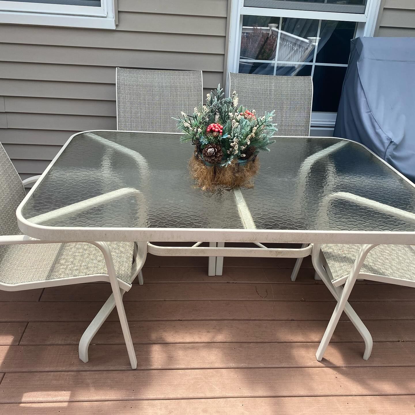 Patio set with glass table and chairs on a wooden deck. A floral arrangement sits in the table center.