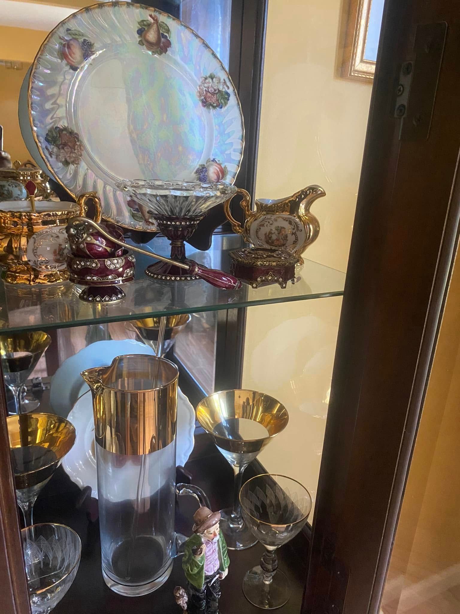 China cabinet with gold-trimmed dishes, glassware, and decorative items on glass shelves.