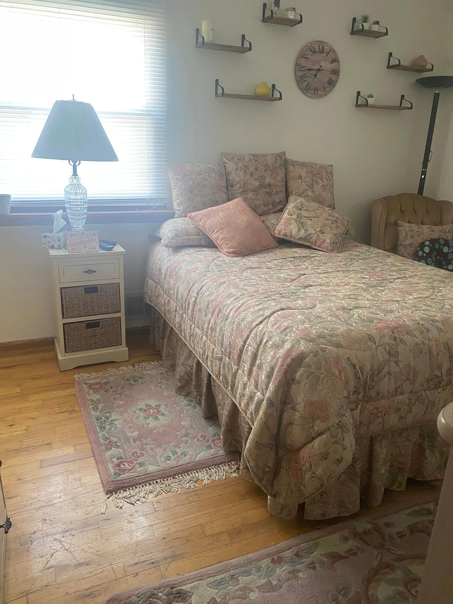 Bedroom with floral bedding, pink rug, and shelves.