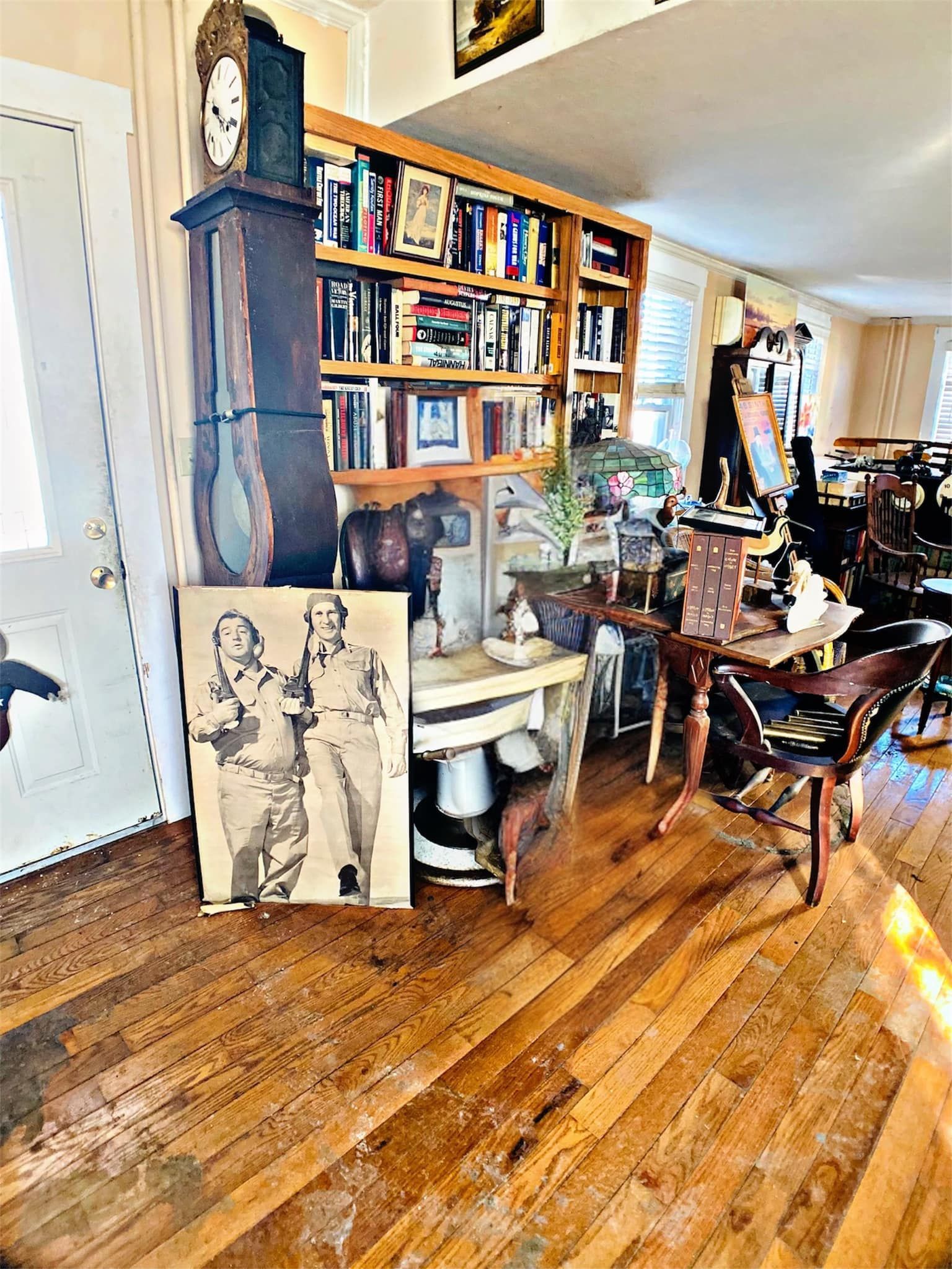 Room interior with hardwood floor, bookshelf, antique clock, and photo of two people.