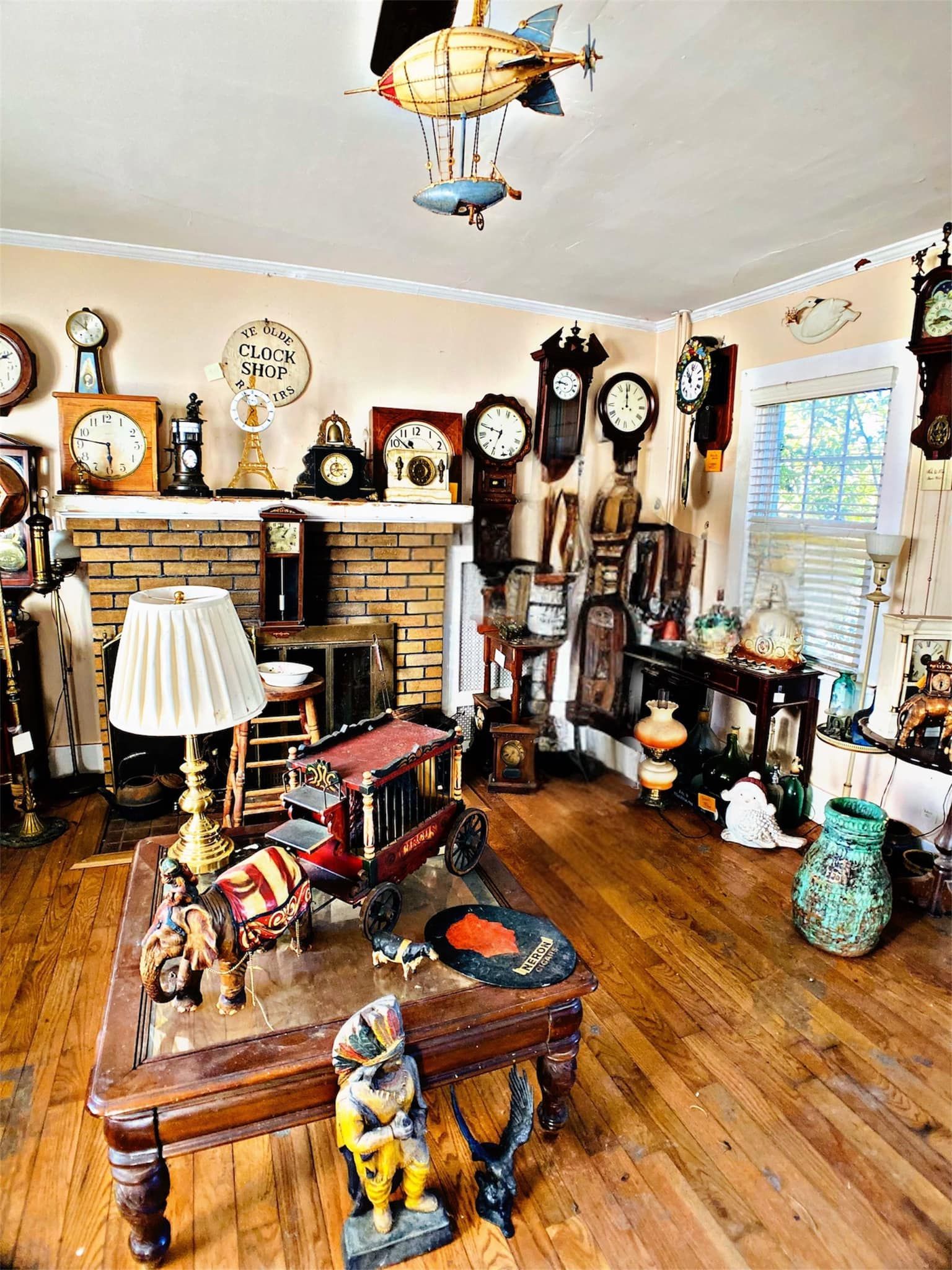 Room filled with antique clocks, a lamp, and decorative objects on a table and around a fireplace.