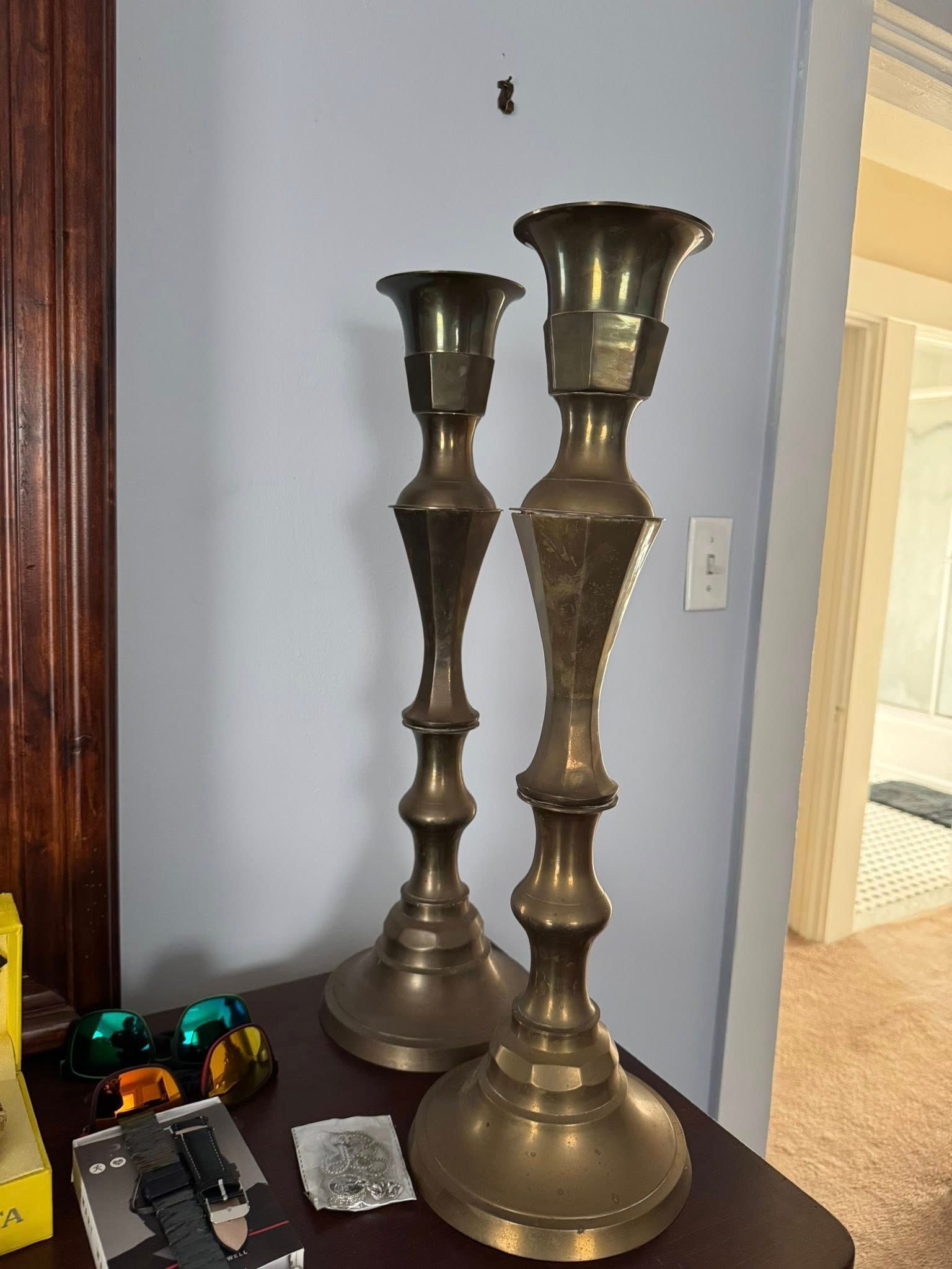 Two tall brass candlesticks on a dark surface, against a light blue wall.