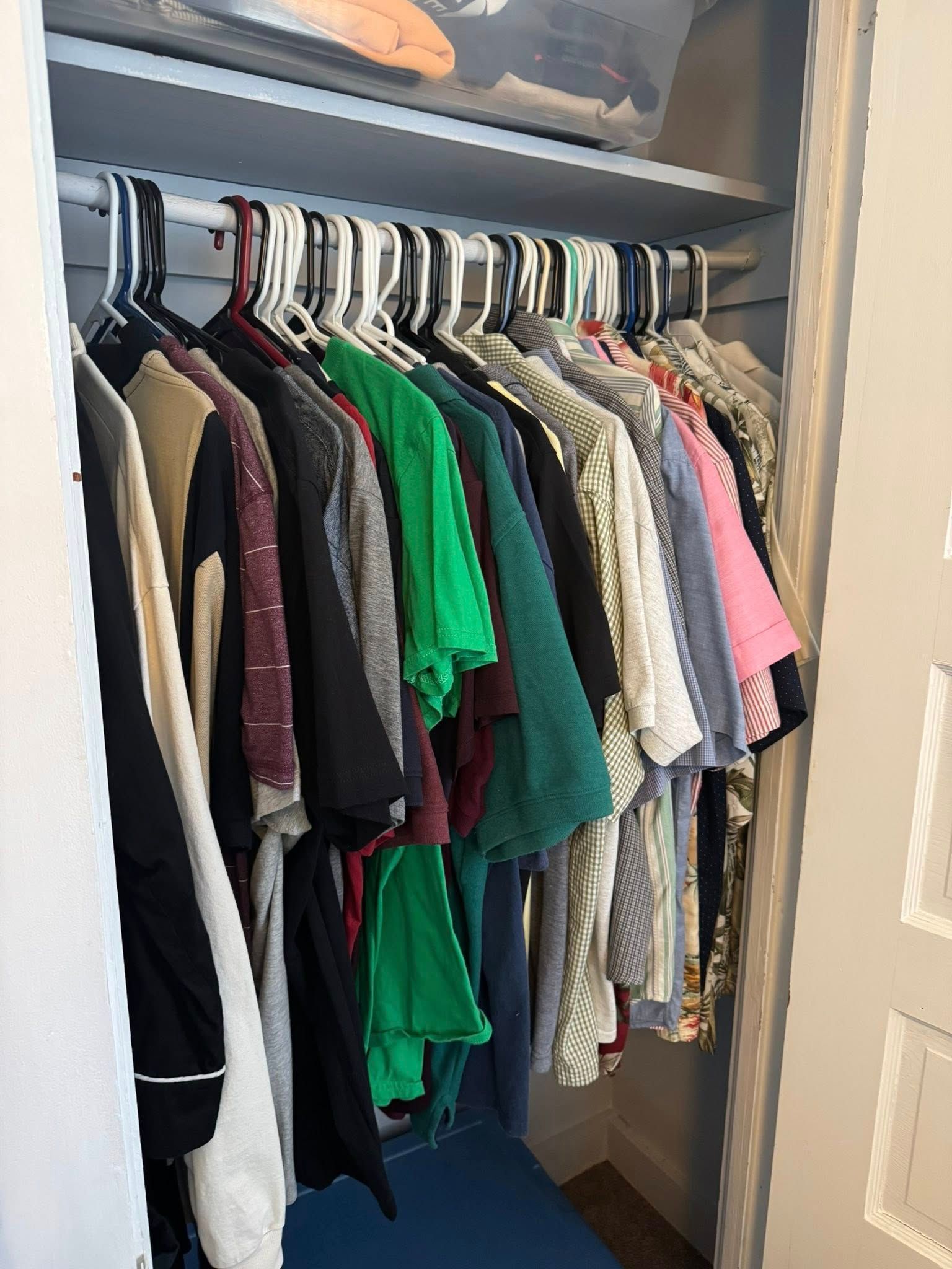 Clothes hanging in a closet; various colors. Top shelf with storage containers.
