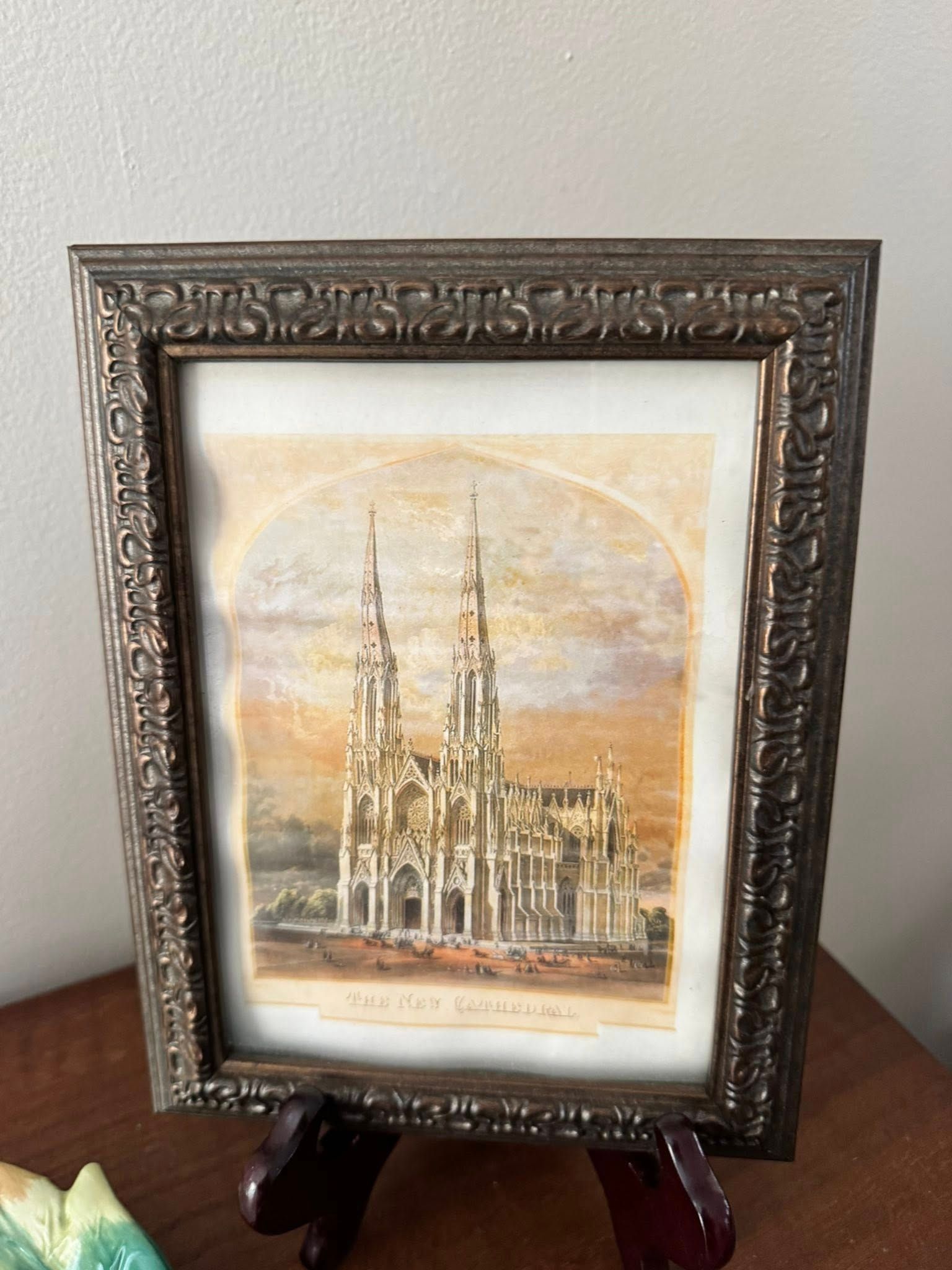 Framed print of a cathedral with tall spires, displayed on a wooden stand against a white wall.