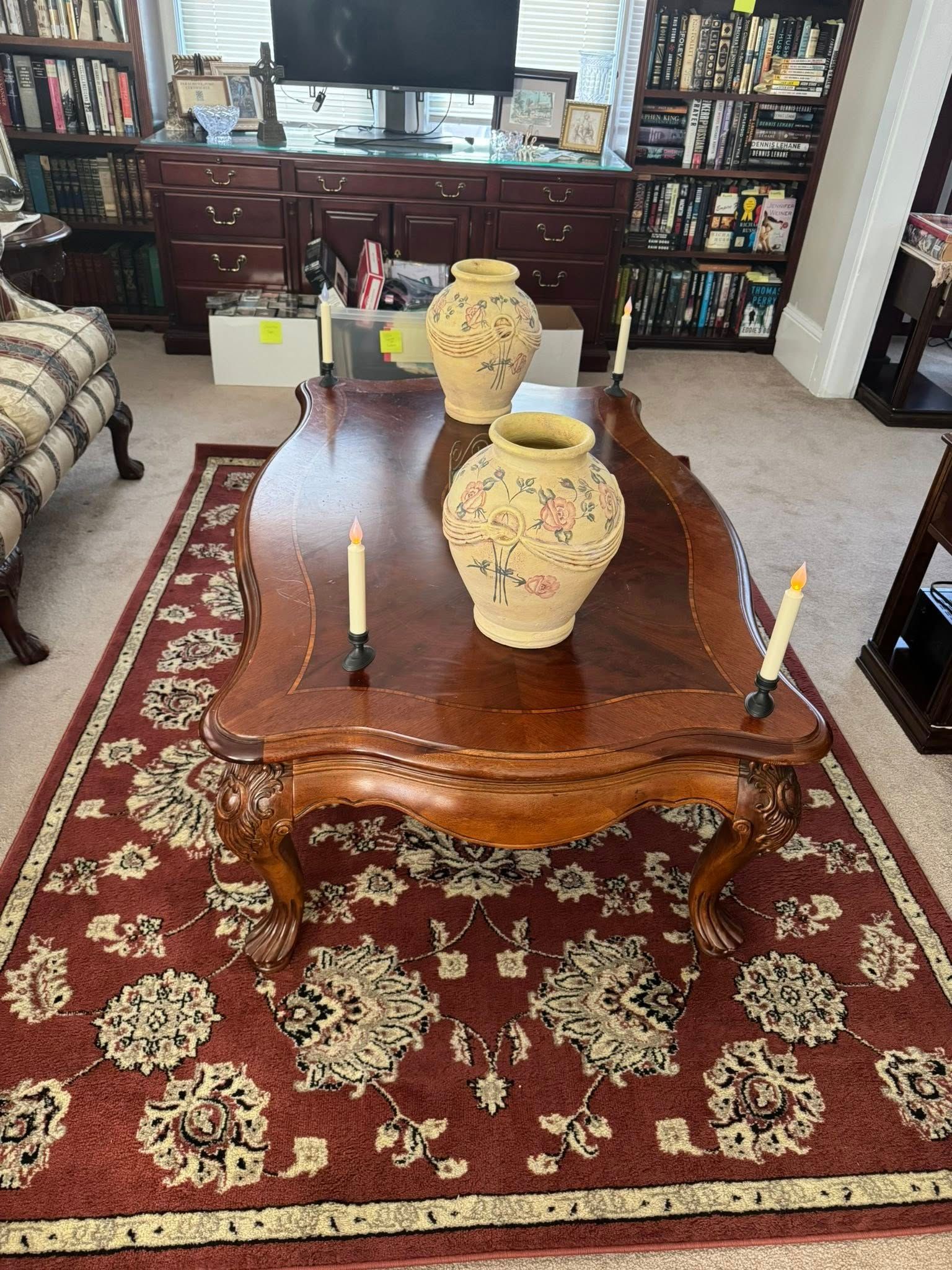 Wooden coffee table with two vases and candles on a patterned red rug.