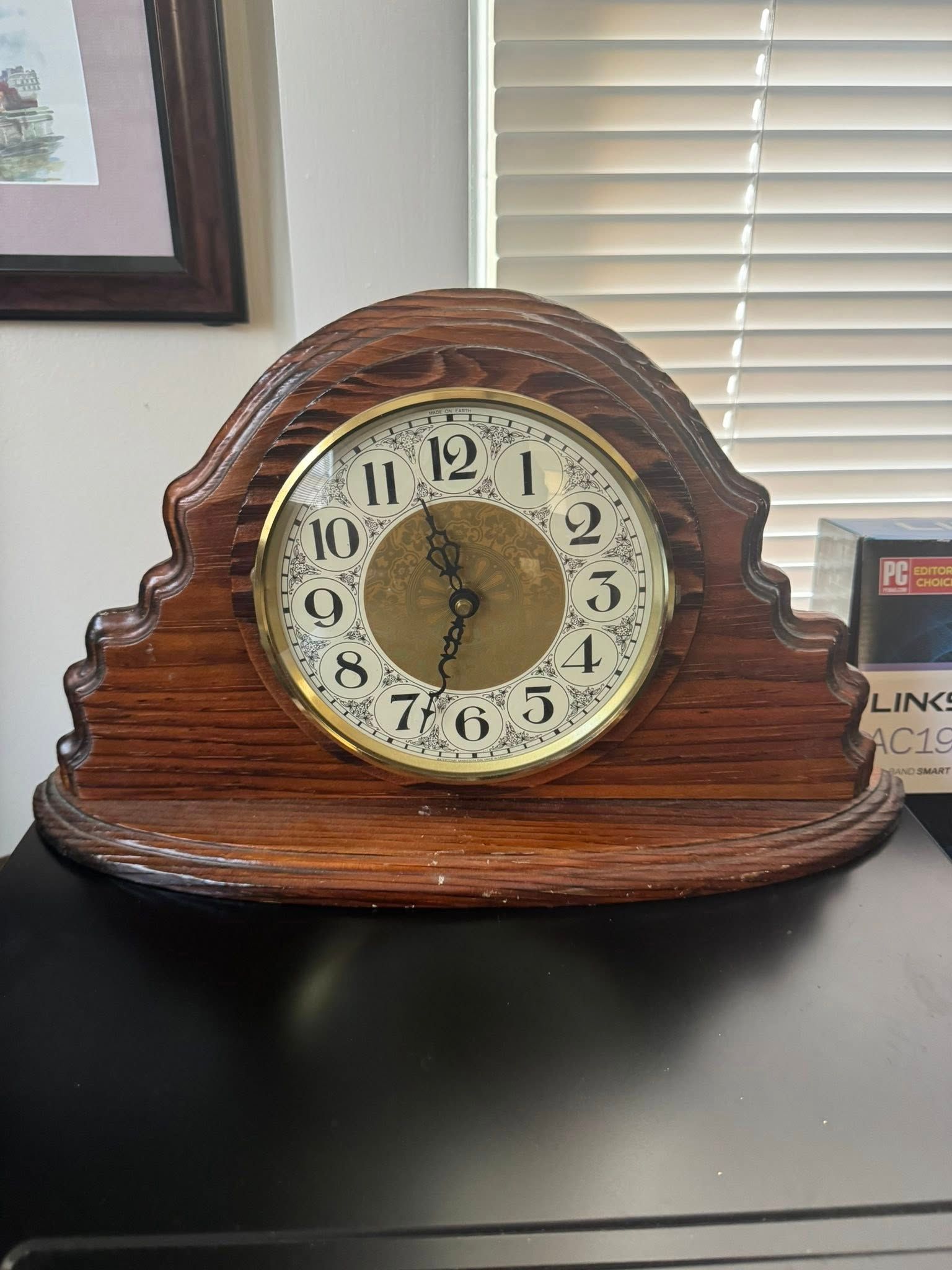 Wooden mantel clock with gold-rimmed face, black numbers, and curved top, on a dark surface.