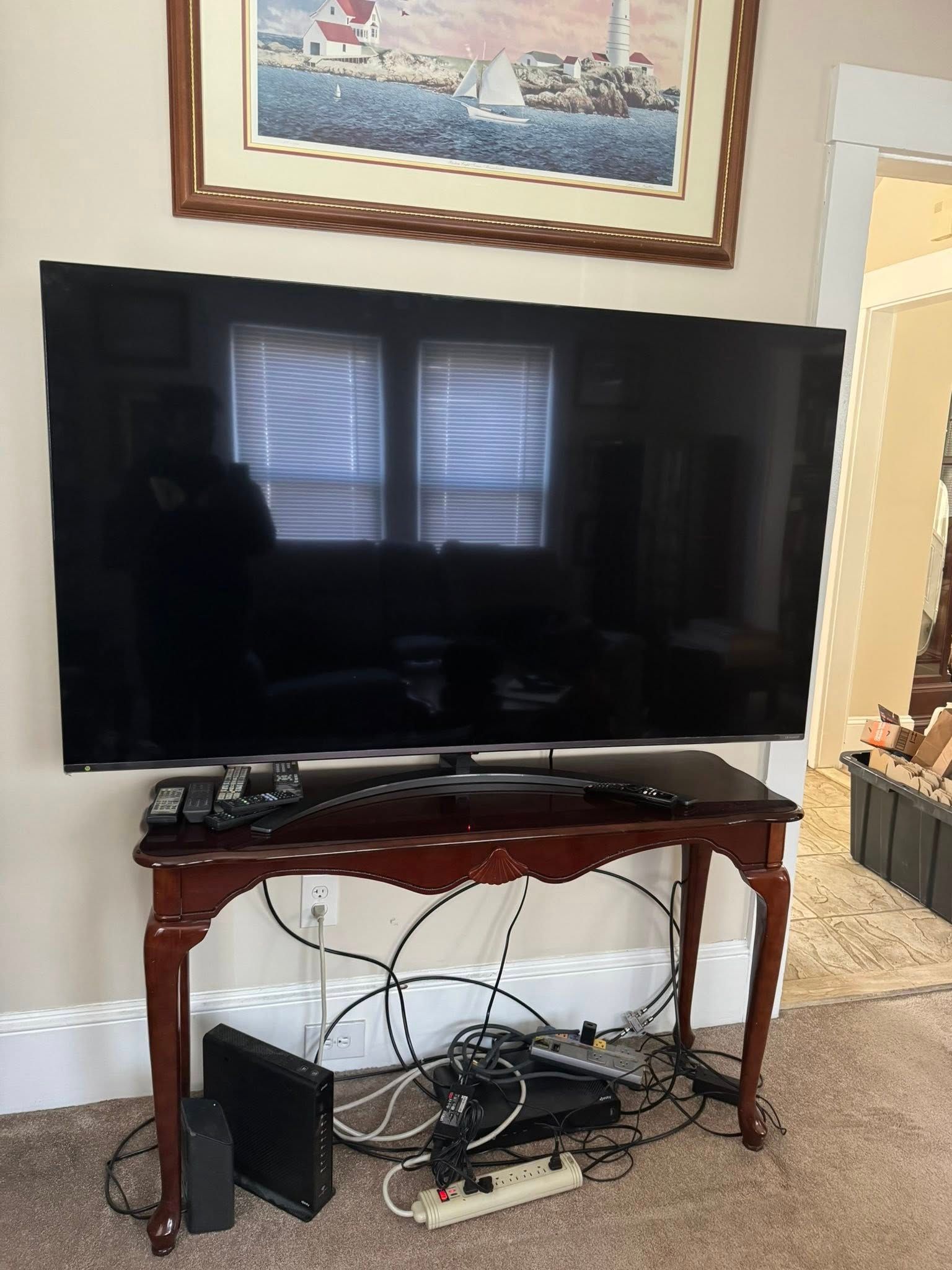 Large TV on a dark wood table with electronics underneath, framed artwork above.