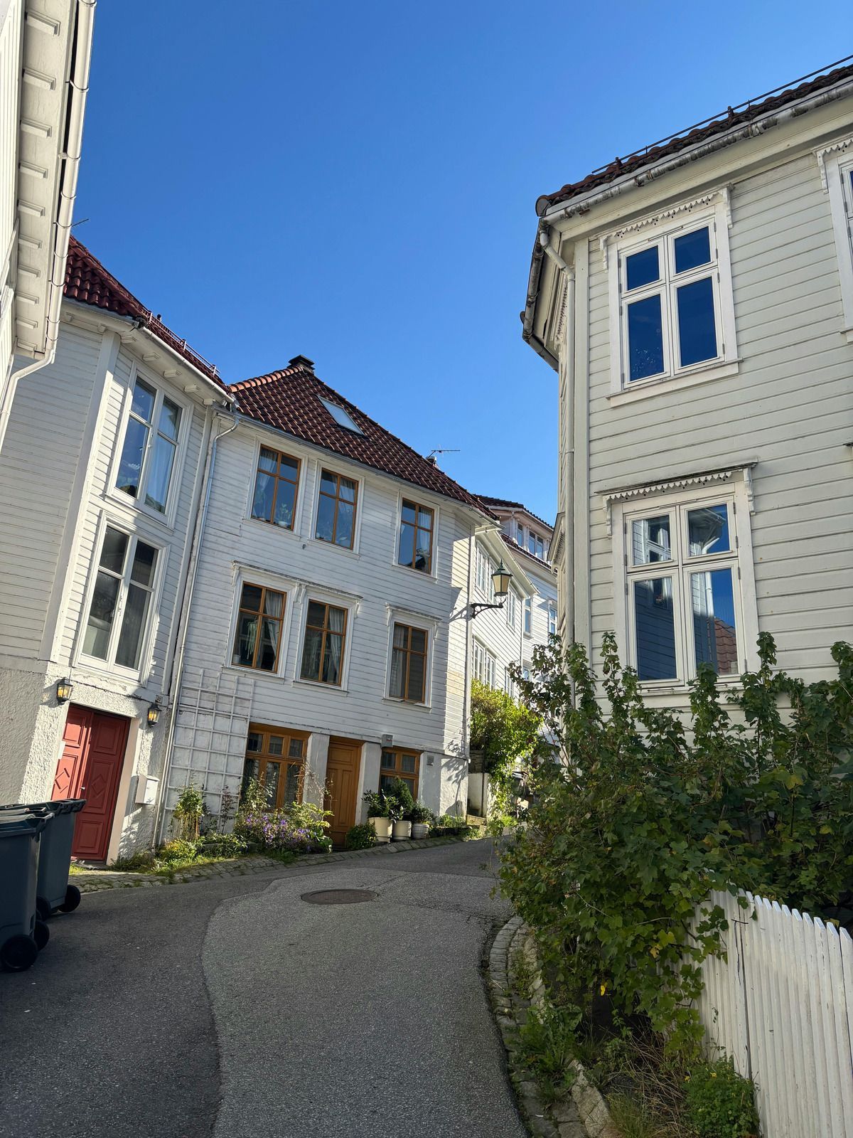Narrow street with white buildings under a blue sky; some buildings have red roofs and doors.