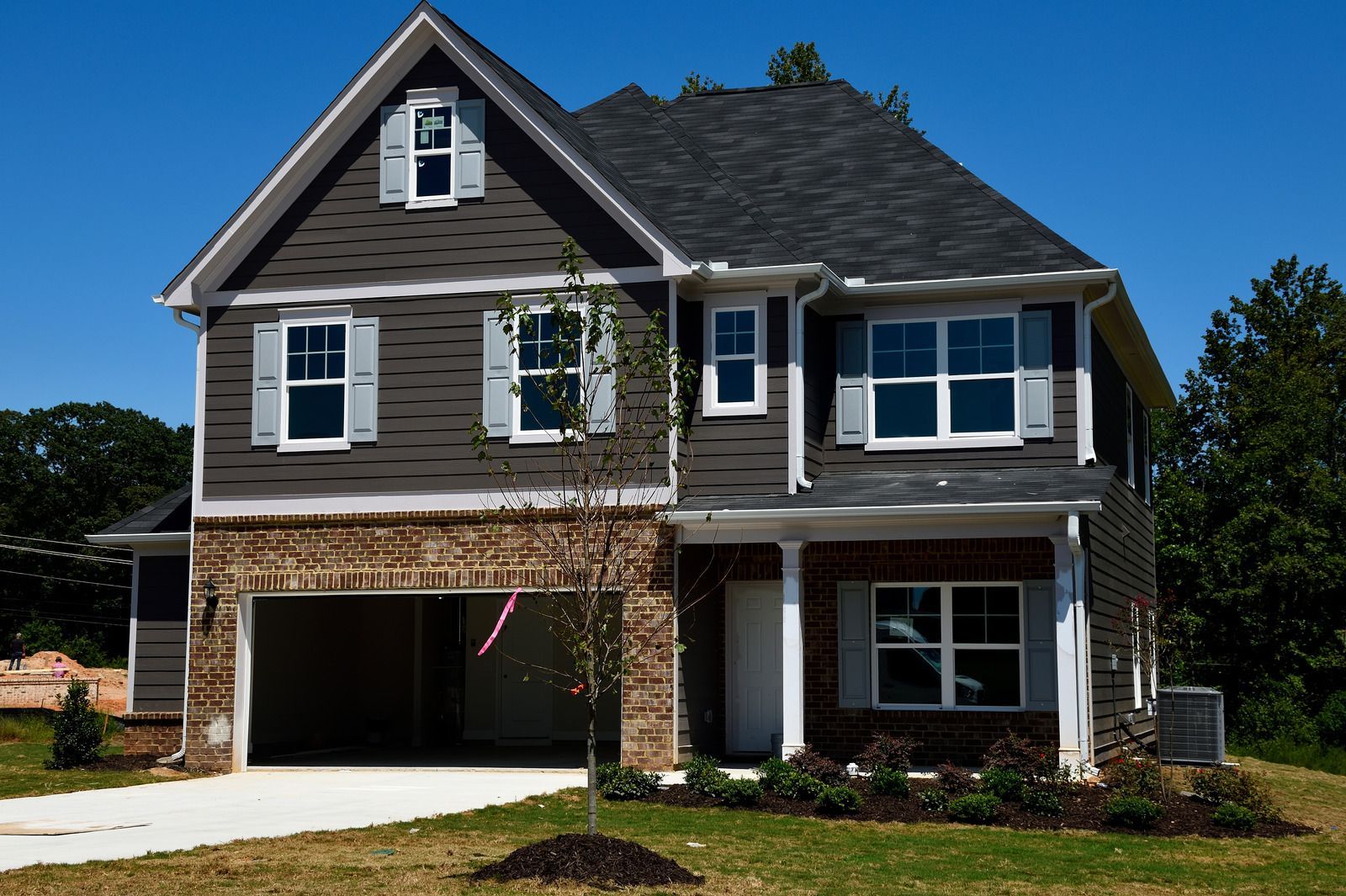 Two-story house with gray siding, brick accents, and open garage under a blue sky.