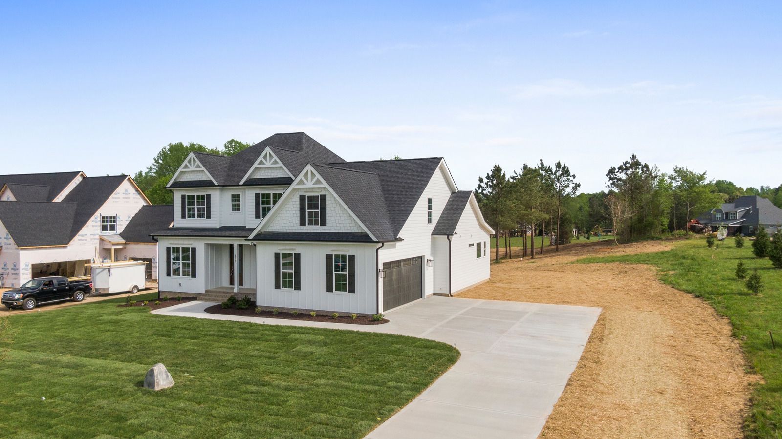 White two-story house with black roof, driveway, and grassy yard in suburban setting.