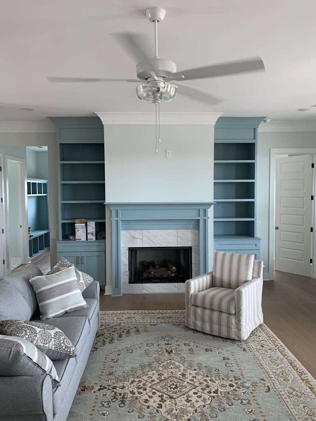 Living room with blue fireplace, bookshelves, and fan, gray couch, striped armchair, and patterned rug.