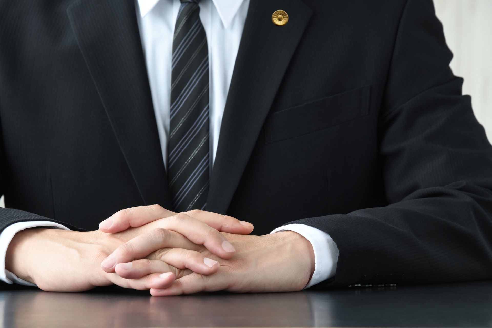 A man in a suit and tie is sitting at a table with his hands folded.