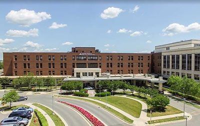 Brick hospital building with landscaped entrance under a blue sky.