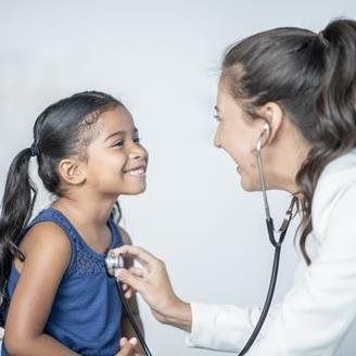Doctor listening to a smiling child's chest with a stethoscope in a clinic setting.