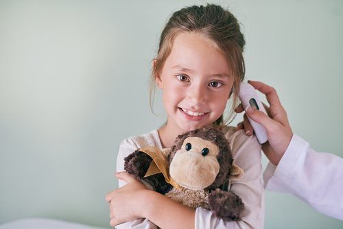 Girl smiling while a thermometer is held to her ear; holding a stuffed monkey.