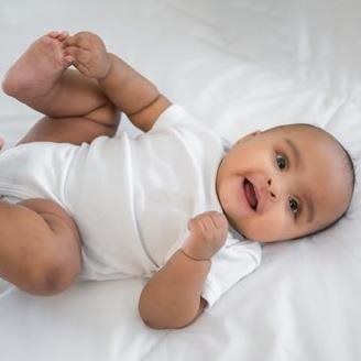 Baby in white onesie lying on white sheet, smiling and looking at the viewer.