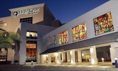 Holy Cross Hospital exterior at dusk, illuminated, with stained glass windows and entrance.