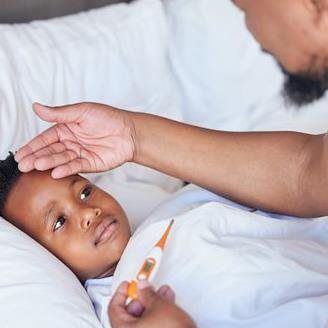 Child in bed with a thermometer, father checking forehead.