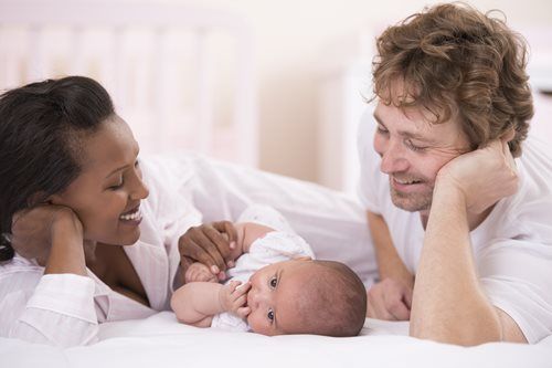 Parents with newborn looking adoringly at baby in bed.
